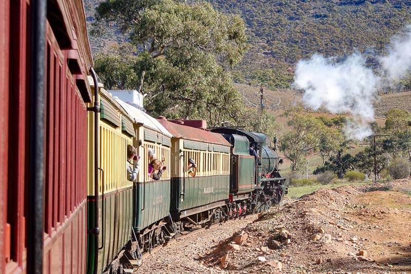 A photo taken leaning out of a train window looking down along the length of the train towards the engine as it curves. There are other people leaning out of windows and a puff of smoke