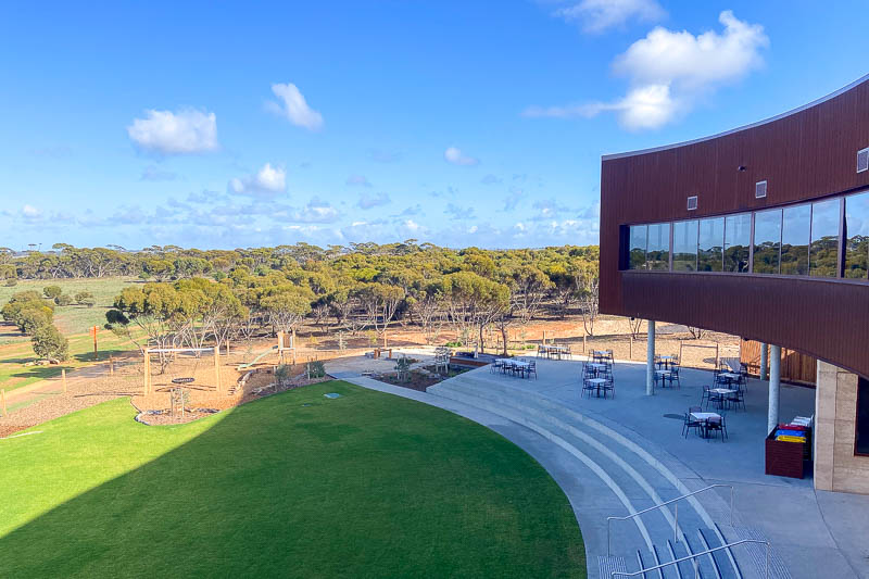 View from a balcony of the curve of the building then across lawn and a playground to the scrub beyond