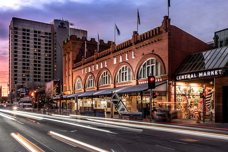A brick building labeled "Federal Hall" sits on a busy street next to Central Market; light trails from passing cars are visible at dusk.